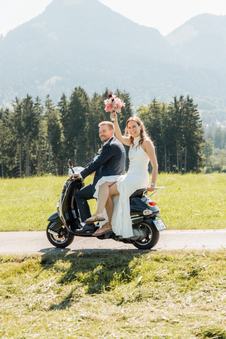 Brautpaar auf der Vespa mit Brautstrauß vor Bergkulisse in den bayerischen Alpen